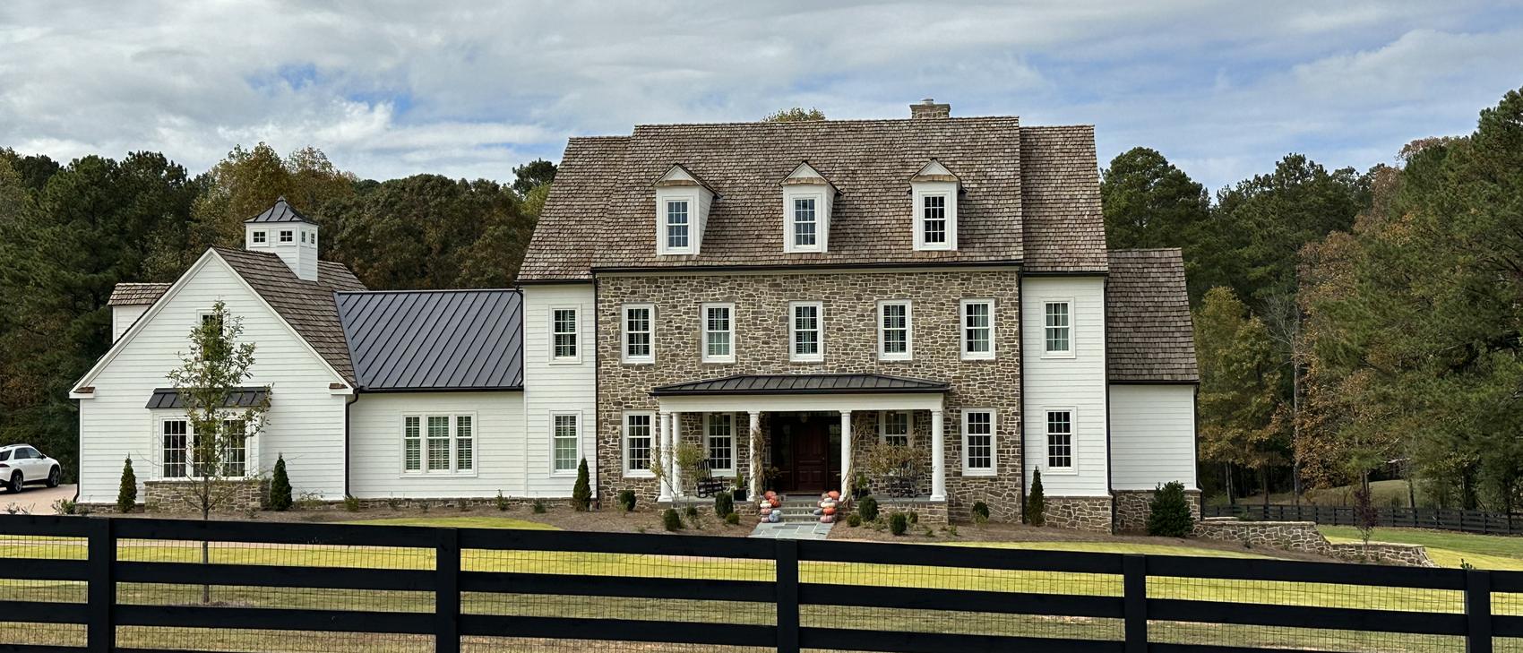 Stone home with cedar shake roof behind a black board fence